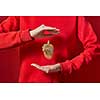 Woman in a red sweatshirt holds beautiful eco Christmas decor golden acorn in hr hands on the same color background with copy space. New Year greeting card.
