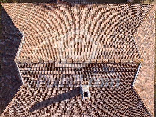 Old tile roof above the house with high chimney and hard shadows from sunny in a summer day. Aerial top view from drone. Old tile roof above the house with high chimney and hard shadows from sunny in a summer day. Aerial top view from drone.