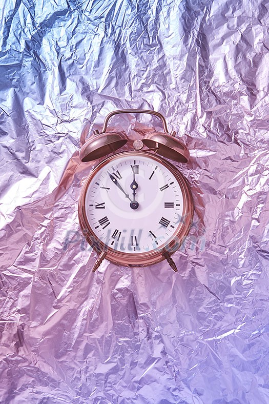 The time is at five minutes to midnight on a painted golden retro alarmclock against abstract shiny pink blue background. Greeting card.