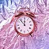 The time is at five minutes to midnight on a painted golden retro alarmclock against abstract shiny pink blue background. Greeting card.