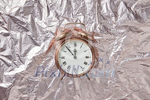 Christmas golden alarmclock on a shiny golden abstract background with copy space. The time is at five minutes to midnight. Greeting card.