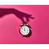 Retro cooper alarm clock with hard shadows from woman's hand on a hot pink background, copy space.