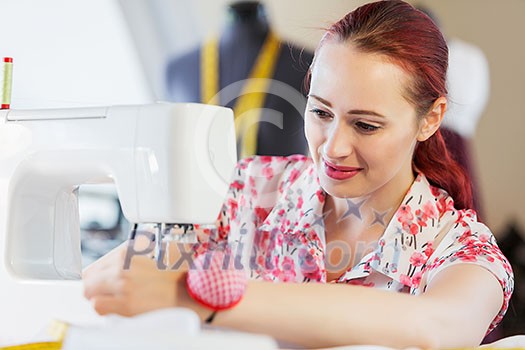 Young attractive woman dressmaker working with sewing machine