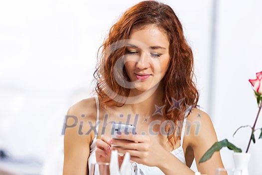 Portrait of young pretty woman sitting at cafe and using mobile phone