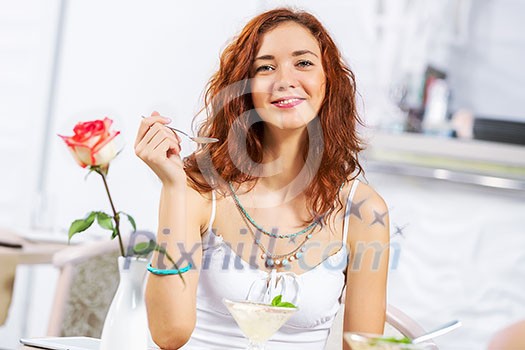 Portrait of young pretty woman sitting at cafe and eating dessert