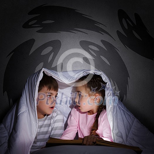 Children sitting in bed under blanket with book Children sitting in bed under blanket with book