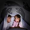 Children sitting in bed under blanket with book