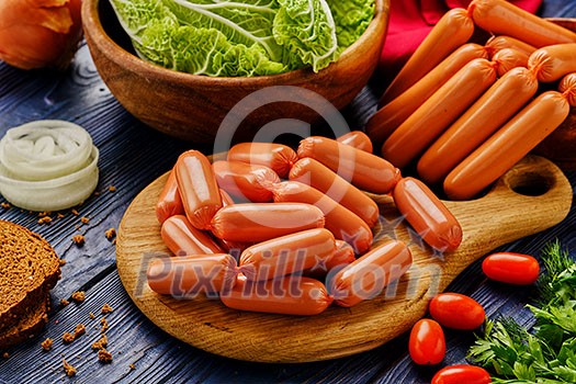 Large bunch of sausages on a cutting board, with bread, herbs, tomatoes and onions.
