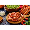 Large bunch of sausages on a cutting board, with bread, herbs, tomatoes and onions.