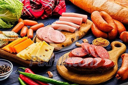 Smoked meat products on a wooden table. Sliced sausage. Sausage with different cheese on the table. Smoked meat products on a wooden table. Sliced sausage. Sausage with different cheese on the table.