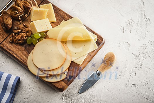 Different varieties of cheese with grapes and walnuts on a wooden board