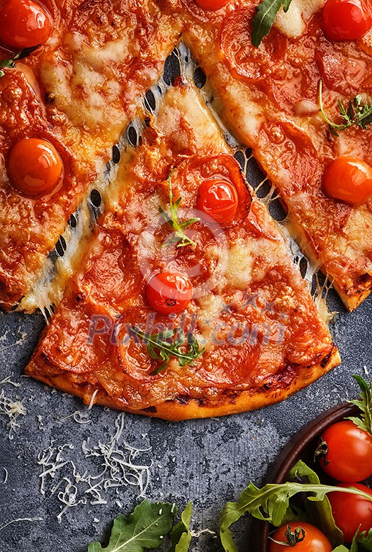 Slice of pepperoni pizza with cherry tomatoes. Sliced tasty pepperoni pizza on the grey stone background. Top view. Close-up.
