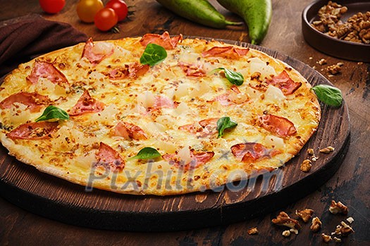 Tasty freshly prepared pizza with pear, nuts and bacon on a wooden board, rustic style.