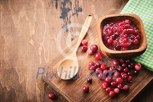 Cranberry jam in a wooden bowl on a wooden background