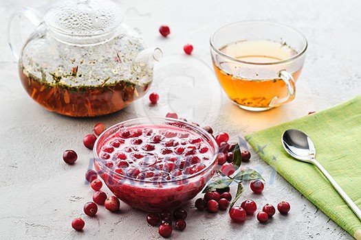 Cranberry jam in a glass bowl and teapot on a white background