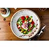 Greek salad with feta cheese, olives and herbs, served in a white plate on a table in a restaurant, view from above.