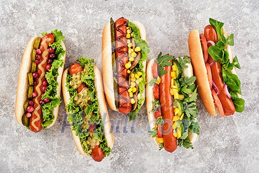 FIve different hot dogs with different toppings on a grey background, overhead view.