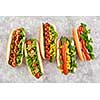 FIve different hot dogs with different toppings on a grey background, overhead view.
