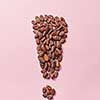 Shape of exclamation point made from natural organic dry cocoa beans on a light pink background with copy space. Effect of improved human brain activity from chocolate.