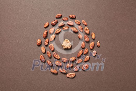 Food frame from fresh dry natural cocoa beans with part of cacao butter in the middle on a brown background, place for text. Flat lay. Dry ingredients for making dark chocolate. Food frame from fresh dry natural cocoa beans with part of cacao butter in the middle on a brown background, place for text. Flat lay. Dry ingredients for making dark chocolate.