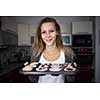 Pretty, young woman baking gluten free cupkes - taking them out of the oven, being pleased with the result