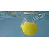 Natural ripe fresh lemon falls into water glass aquarium with splashing on a gray background. Slow motion 2K video.
