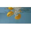 Glass aquarium with floating halves of fresh natural orange in the water with air bubles on a gray background. Slow motion 2K video.