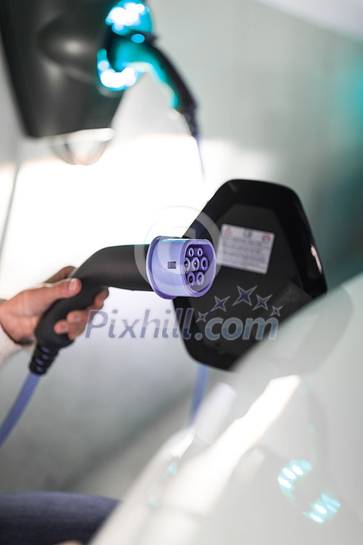 Young woman charging an electric vehicle in an underground garage equiped with e-car charger. Car sharing concept.