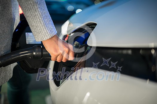 Young woman charging an electric vehicle. Car sharing concept.