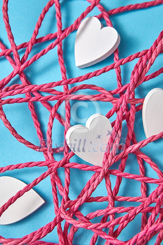 Happy holiday close up composition with red tangled rope and small white painted wooden hearts on a light blue background. Valentine's greeting card. Happy holiday close up composition with red tangled rope and small white painted wooden hearts on a light blue background. Valentine's greeting card.