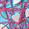 Happy holiday close up composition with red tangled rope and small white painted wooden hearts on a light blue background. Valentine's greeting card.