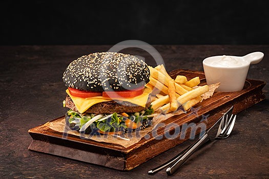 Delicious fresh juicy homemade cheeseburger in a black bun with tomatoes and salad. Beef Burger with Cheese and Vegetables