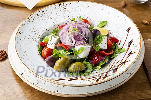 Greek salad with feta cheese, olives and herbs, served in a white plate on a table in a restaurant