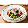 Greek salad with feta cheese, olives and herbs, served in a white plate on a table in a restaurant