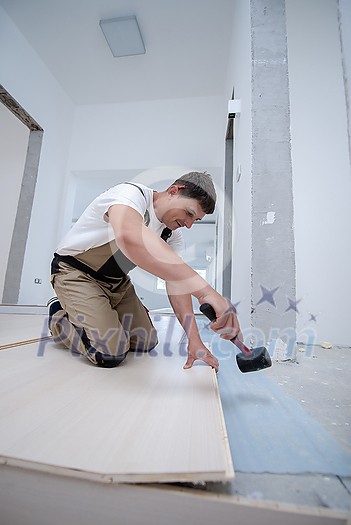 professional carpenter using rubber hammer while installing new laminated wooden floor in a unfinished apartment professional carpenter using rubber hammer while installing new laminated wooden floor in a unfinished apartment