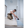 professional carpenter using rubber hammer while installing new laminated wooden floor in a unfinished apartment