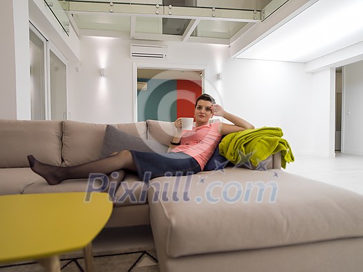 young woman enjoying free time drinking tea while relaxing on corner sofa at big stylish duplex apartment young woman enjoying free time drinking tea while relaxing on corner sofa at big stylish duplex apartment
