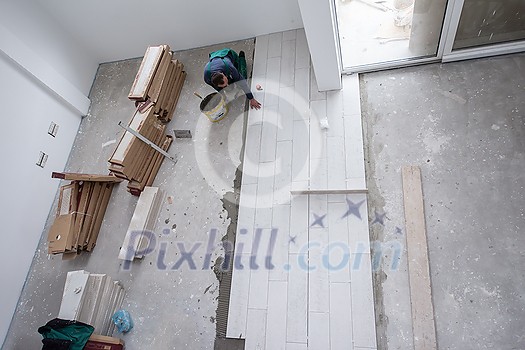 skilled worker installing the ceramic wood effect tiles on the floor Worker making laminate flooring on the construction site of the new apartment skilled worker installing the ceramic wood effect tiles on the floor Worker making laminate flooring on the construction site of the new apartment
