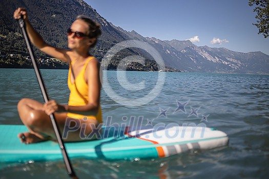 SUP Stand up paddle board concept - Pretty, young woman paddle boarding on a lovely lake in warm late afternoon light - shot from underwater