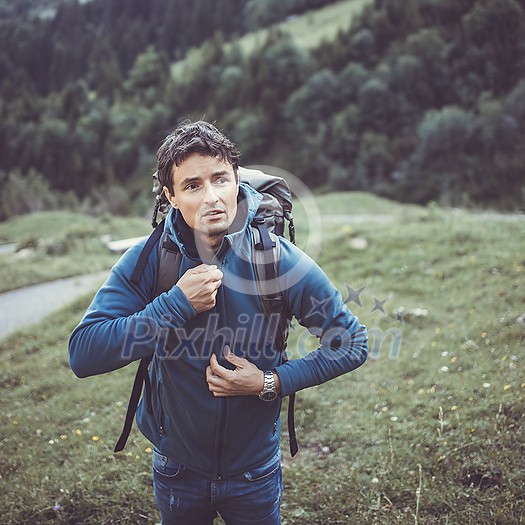Young man in the mountains during an outdoor advernture/expedition, zipping his jacket as the evening cold is setting in