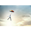 Young businessman flying high in sky on umbrella