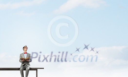 Young businessman wearing red bow tie sitting on bench with book in hands