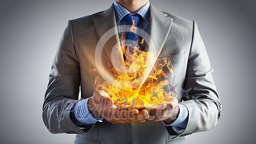 Young businessman holding fire flames in palms Young businessman holding fire flames in palms