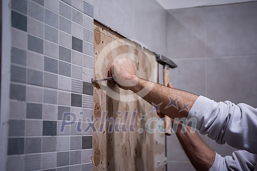 professional worker remove demolish old tiles in a bathroom with hammer and chisel