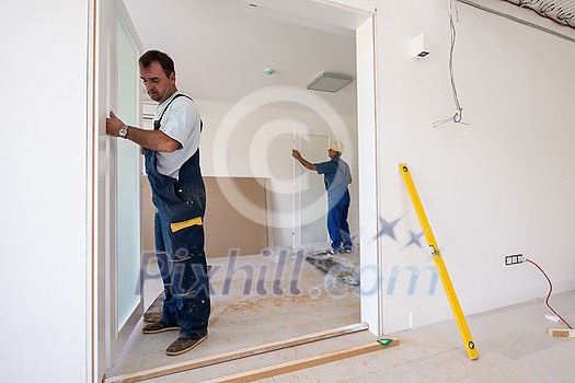 male workers carpenters installing interior glass door with a wooden frame at new luxury apartment male workers carpenters installing interior glass door with a wooden frame at new luxury apartment