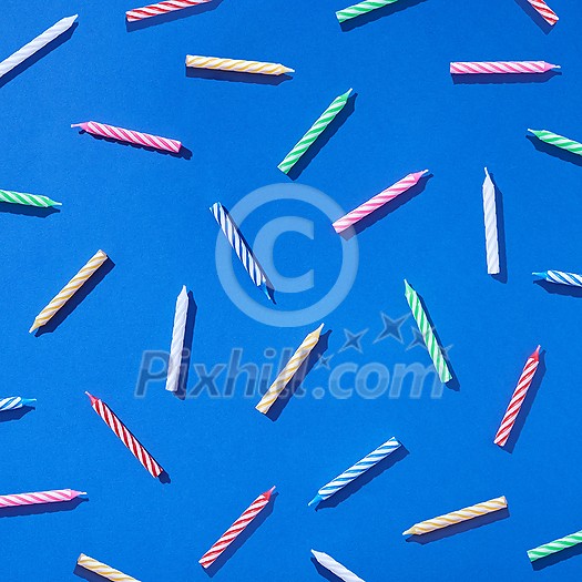 Pattern from multicolored candles for cake on a blue background with hard shadows. Birthday party card composition. Flat lay.