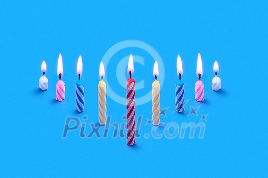 Greeting card from perspective composition of burning festive candles for cakes and sweet dessert on a blue background, copy space.
