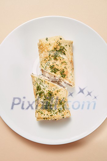 Delicious homemade pancake rolled with filling from chicken, natural mushroom and white sauce on a ceramic plate on a pastel beige background, copy space. Top view. Delicious homemade pancake rolled with filling from chicken, natural mushroom and white sauce on a ceramic plate on a pastel beige background, copy space. Top view.
