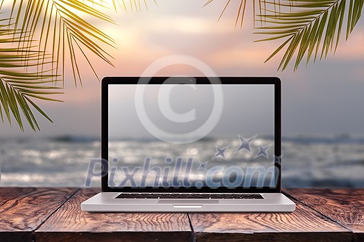 Notebook monitor with blurred seascape sunrise picture on a wooden table against the same background with green palm leaves frame, copy space. Working at sea, outside office concept.