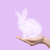 A rabbit made of a cloud is held in the hand by a woman on a pink background. Easter concept. As a gift for the holiday
